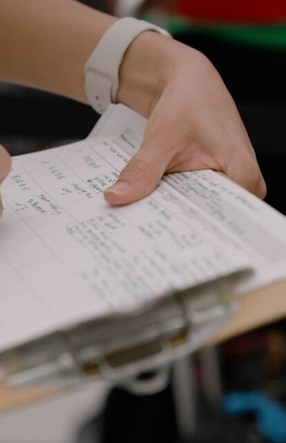 Photograph of a person holding a clipboard and pen, writing down data.