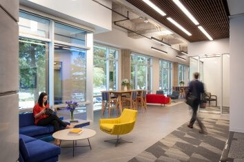 Interior photo of CityView Repositioning. A woman reads on a blue couch while a man walks by her past a yellow chair 